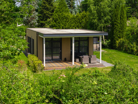 Vogellodge with hot tub, surrounded by lush greenery, outdoor seating on a covered terrace, peaceful view.