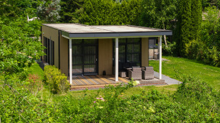 Vogellodge met hot tub, omgeven door groene natuur, overdekt terras met zitmeubilair, rustgevend uitzicht.
