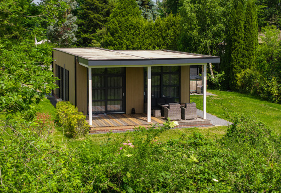 Vogellodge met hot tub, omgeven door groene natuur, overdekt terras met zitmeubilair, rustgevend uitzicht.