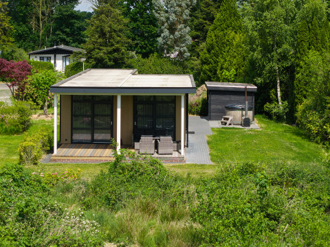 Small lodge with covered terrace and hot tub surrounded by greenery at Holiday Resort 't Schuttenbelt, Netherlands.