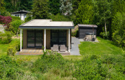 Small lodge with covered terrace and hot tub surrounded by greenery at Holiday Resort 't Schuttenbelt, Netherlands.
