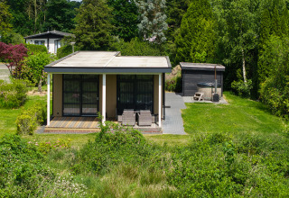 Kleine lodge met overdekt terras en hottub, omringd door natuur, op Holiday Resort 't Schuttenbelt in Nederland.