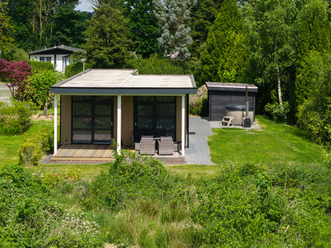 Pequeña cabaña con terraza cubierta y jacuzzi rodeada de vegetación en Holiday Resort 't Schuttenbelt, Países Bajos.