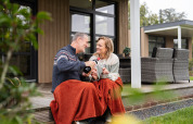 Ein Paar genießt ein Glas Wein auf der Terrasse mit Decke an der Vogellodge + Hot Tub im 't Schuttenbelt, Niederlande.