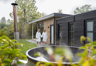 Zwei Personen im Bademantel draußen bei der Vogellodge mit Hot Tub im Holiday Resort 't Schuttenbelt, Niederlande.