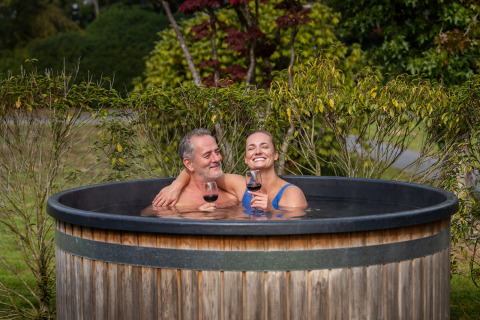 Pareja disfruta de vino en un jacuzzi exterior en Terrace Lodge + sauna en Holiday Resort 't Schuttenbelt, Países Bajos.
