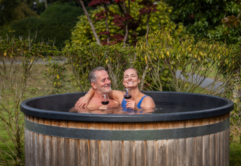 Coppia rilassata con vino nella vasca idromassaggio alla Terrace Lodge + sauna a Holiday Resort 't Schuttenbelt, Paesi Bassi.