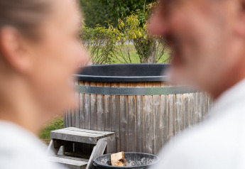 Pareja desenfocada con albornoces blancos ante sauna y jacuzzi privados en ‘t Schuttenbelt, Países Bajos.