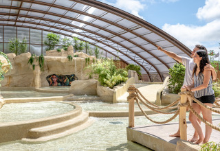 Couple admiring the indoor water park and lush greenery at Flower Camping Au Bois Des Biches in France.