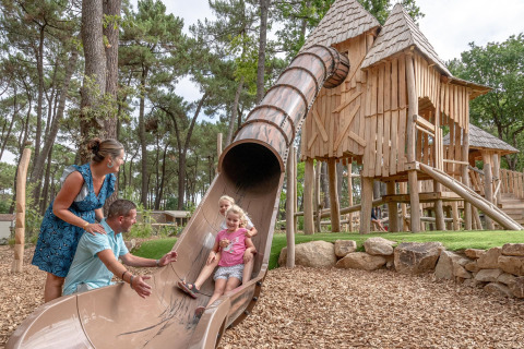 Gezin geniet van speeltuin met glijbaan en houten hutten bij Flower Camping Au Bois Des Biches, Frankrijk.