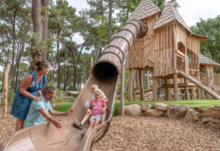 Gezin geniet van speeltuin met glijbaan en houten hutten bij Flower Camping Au Bois Des Biches, Frankrijk.