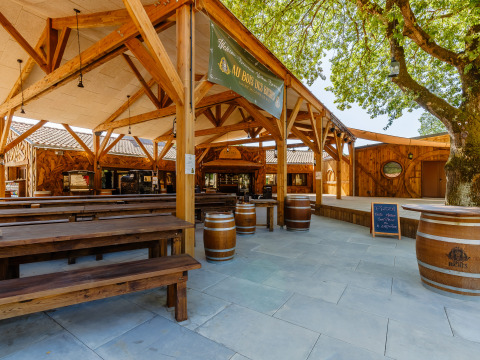 Outdoor dining area with wooden benches and barrels at Flower Camping Au Bois Des Biches, Pays de la Loire, France.