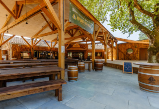 Outdoor dining area with wooden benches and barrels at Flower Camping Au Bois Des Biches, Pays de la Loire, France.