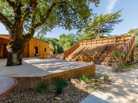 Escenario y gradas de madera al aire libre en Flower Camping Au Bois Des Biches, rodeado de árboles en Pays de la Loire.