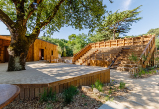Escenario y gradas de madera al aire libre en Flower Camping Au Bois Des Biches, rodeado de árboles en Pays de la Loire.