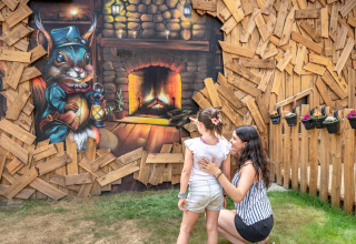 Une femme et une enfant regardent une fresque représentant un écureuil de conte de fées près d'une cheminée en bois.