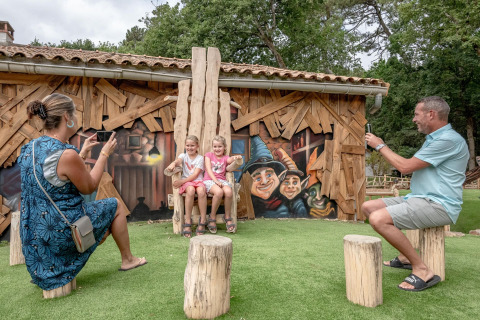 Genitori fotografano due bambine sedute su una sedia di legno davanti a un murale colorato in un parco vacanze.