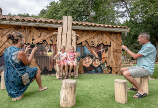 Forældre tager billeder af to børn, der sidder på en træstol foran farverig vægkunst i en feriepark.