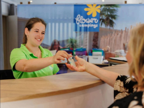 Recepcionista entregando una llave a un huésped en Flower Camping Au Bois Des Biches, Pays de la Loire, Francia.