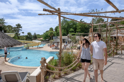 Couple walking by the pool at Flower Camping Au Bois Des Biches holiday park in Pays de la Loire, France.