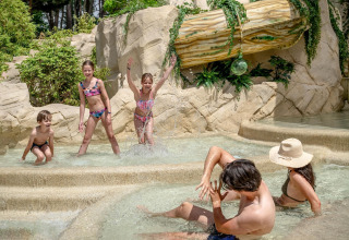 Children and adults enjoy a tropical pool with rocks and plants at Flower Camping Au Bois Des Biches, France.