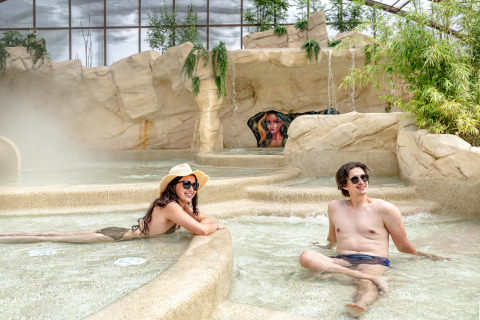 Zwei Erwachsene entspannen sich im Indoor-Spa-Bereich mit Felsen im Flower Camping Au Bois Des Biches in Frankreich.