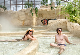 Zwei Erwachsene entspannen sich im Indoor-Spa-Bereich mit Felsen im Flower Camping Au Bois Des Biches in Frankreich.