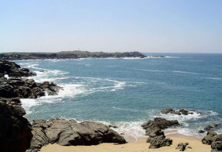 Vista costera en Flower Camping Au Bois Des Biches en Pays de la Loire, Francia, con rocas, arena y olas.