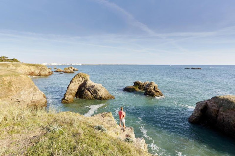 Ein Mann steht auf einem Felsen am Meer im Flower Camping Au Bois Des Biches in Pays de la Loire, Frankreich.