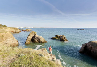 Mand står på klippe ved havet i Flower Camping Au Bois Des Biches, Pays de la Loire, Frankrig, med udsigt over vandet.