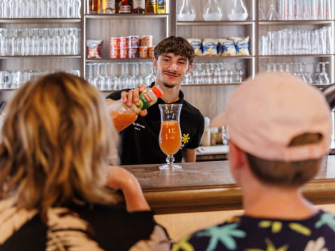 Barman servant une boisson à deux clients au bar du Flower Camping Au Bois Des Biches en Pays de la Loire, France.
