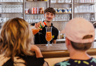Barista serve una bevanda a due ospiti al bar al Flower Camping Au Bois Des Biches in Pays de la Loire, Francia.