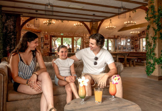 Eine Familie entspannt sich auf einem Sofa mit Getränken im Flower Camping Au Bois Des Biches, Pays de la Loire, Frankreich.