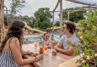 Una familia disfruta de bebidas en una mesa junto a la piscina en Flower Camping Au Bois Des Biches, Francia.