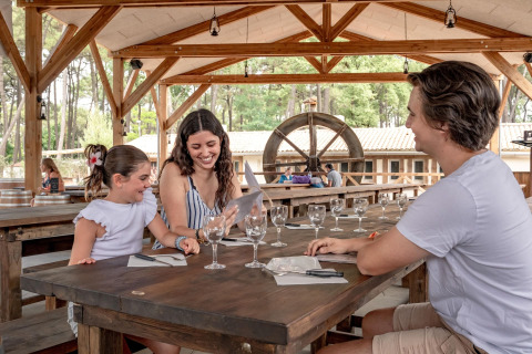 Famille souriante partageant un moment à une table en bois au Flower Camping Au Bois Des Biches, France.