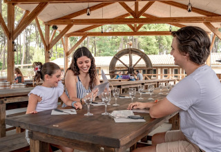 Familie genießt ein gemeinsames Essen an einem Holztisch im Flower Camping Au Bois Des Biches, Frankreich.