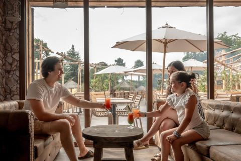 Familia disfrutando bebidas en una terraza acogedora con sombrillas en Flower Camping Au Bois Des Biches, Francia.