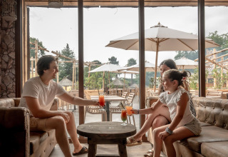 Famiglia si gode bibite insieme in terrazza al Flower Camping Au Bois Des Biches, Pays de la Loire, Francia.