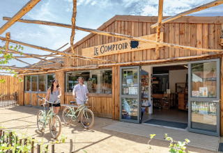 Zwei Personen mit Fahrrädern vor Le Comptoir im Flower Camping Au Bois Des Biches in Pays de la Loire, Frankreich.