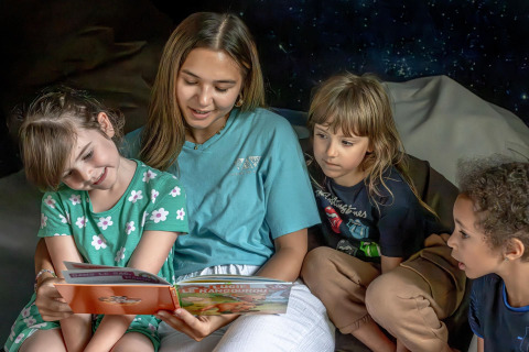 Un adulto lee un libro ilustrado a tres niños en Flower Camping Au Bois Des Biches, Pays de la Loire, Francia.