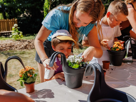 Children and adults planting and watering flowers together at an outdoor workshop in France holiday park.