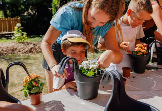 Kinderen en volwassenen planten en geven samen bloemen water bij een buitenactiviteit in Frankrijk.