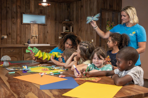 Kinderen knutselen met volwassenen in een houten kamer bij Flower Camping Au Bois Des Biches, Frankrijk.