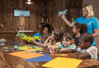 Kinderen knutselen met volwassenen in een houten kamer bij Flower Camping Au Bois Des Biches, Frankrijk.