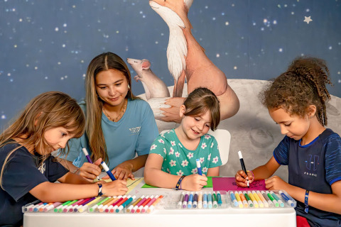 Niños y una adulta dibujando con rotuladores en una mesa en Flower Camping Au Bois Des Biches, Pays de la Loire, Francia.