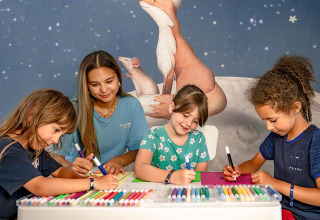 Kinderen en een volwassene kleuren samen met stiften aan een tafel bij Flower Camping Au Bois Des Biches, Frankrijk.