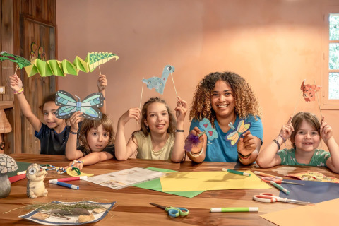 Kinder und eine Betreuerin basteln mit Papier und Stiften im Flower Camping Au Bois Des Biches, Frankreich.