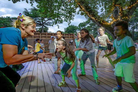 Kinderen dansen en spelen samen met een volwassene op een houten terras in een Frans vakantiepark tussen de bomen.