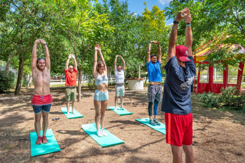 Eine Gruppe Menschen macht Outdoor-Fitness oder Yoga auf Matten in einem sonnigen, grünen Park.