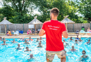 Een redder met rood shirt geeft watergymnastiekles in een openluchtzwembad bij zonnig weer.